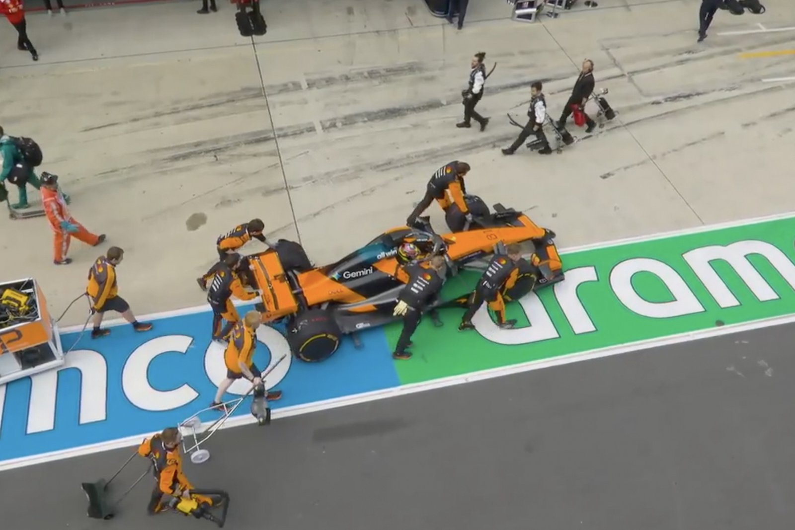 Oscar piastri's mclaren being pushed back into the garage by a group of mechanics